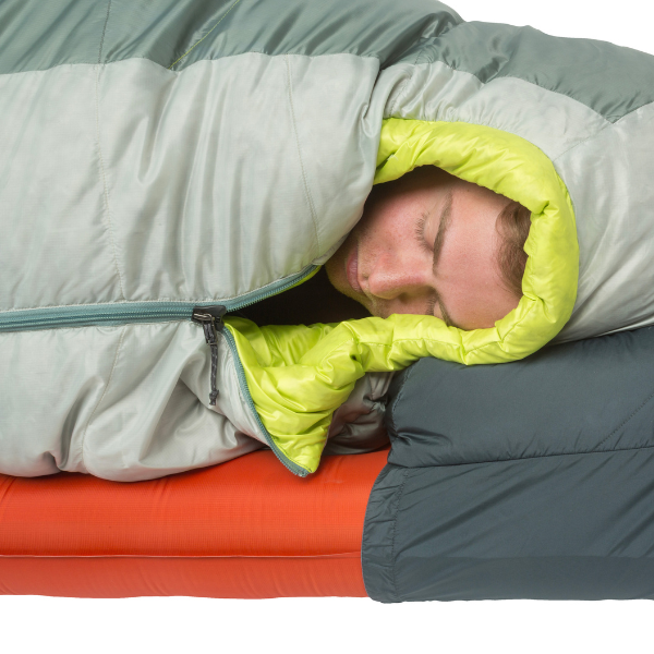 Person sleeping in a gray and green sleeping bag on an orange sleeping pad.