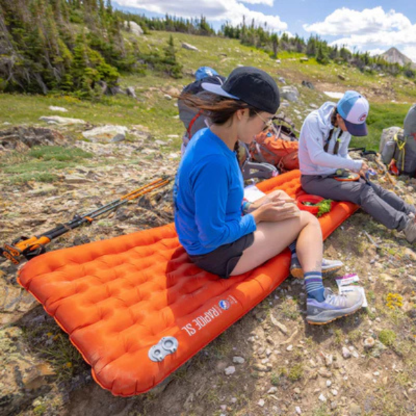 People sitting on orange sleeping pads in a mountainous area